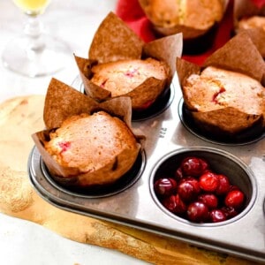 The muffins are in a muffin tin and one of the muffin tins is filled with cranberries