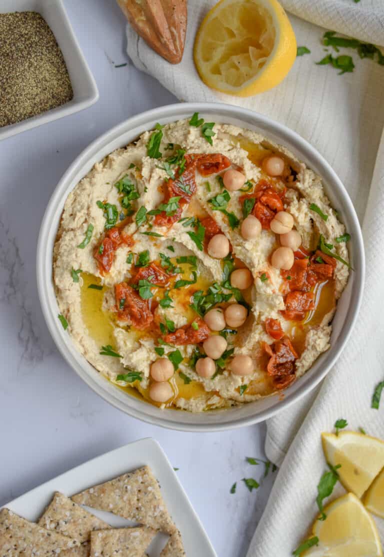 An overhead shot of a bowl of hummus topped with sun dried tomatoes