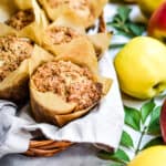 A close up of one of the apple streusel sourdough muffin surrounded by apples