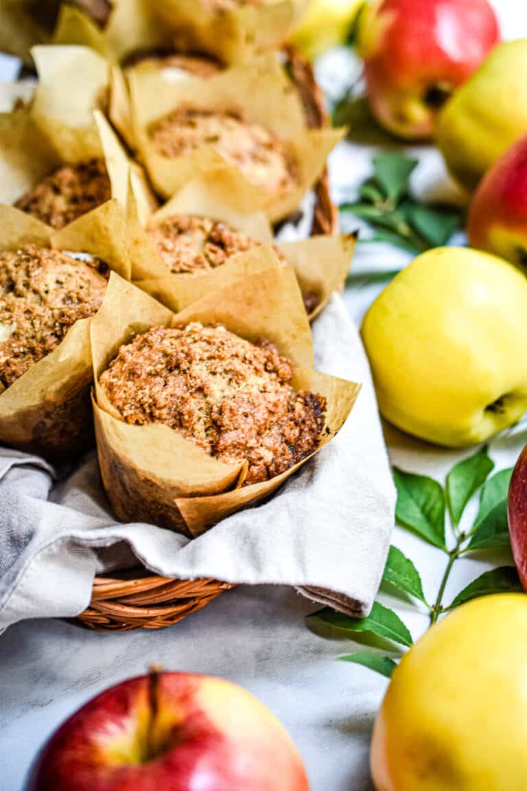 A close up of one of the apple streusel sourdough muffin surrounded by apples