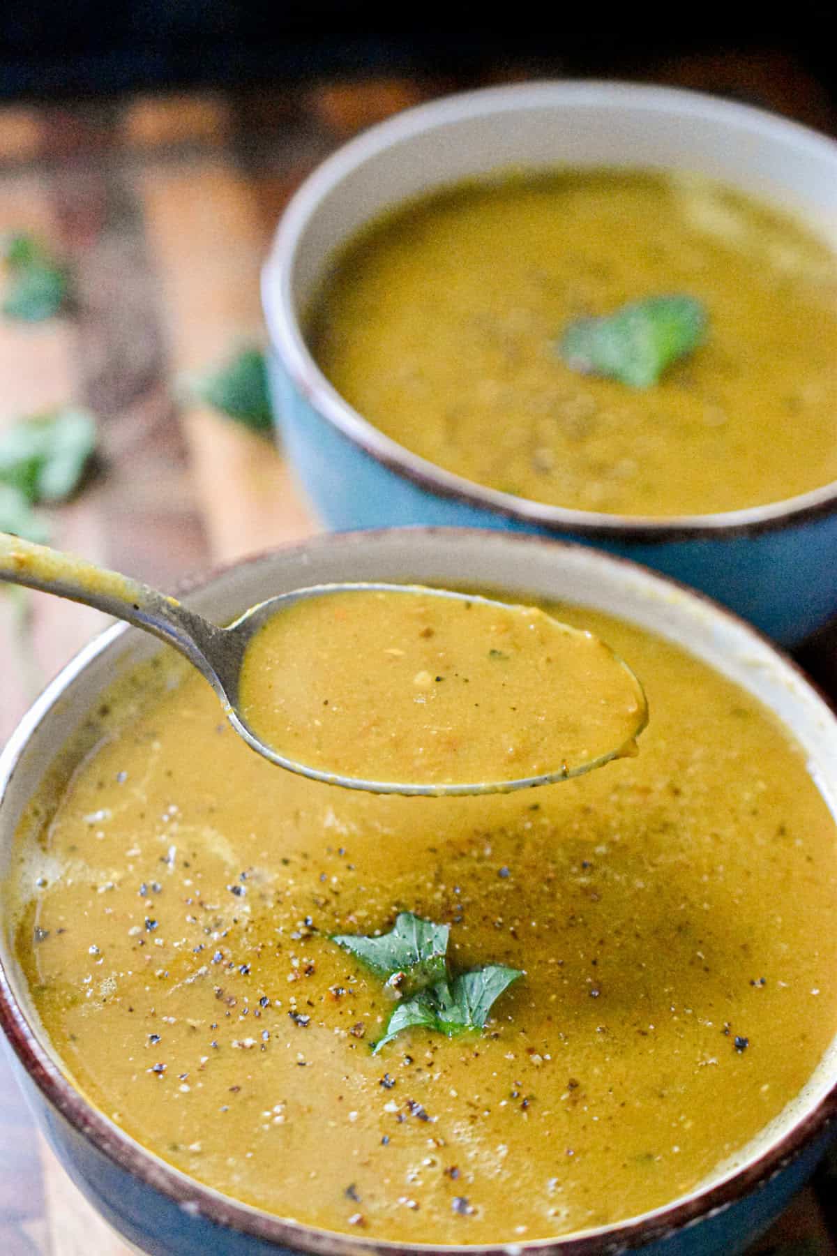 Two bowls of instant pot lentil soup is topped with a cilantro leaf and a spoon is taking some of the soup out of the bowl.