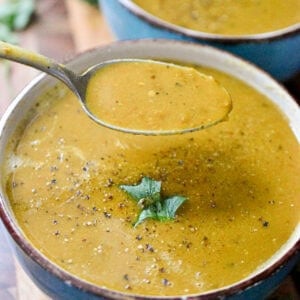 Two bowls of instant pot lentil soup is topped with a cilantro leaf and a spoon is taking some of the soup out of the bowl.