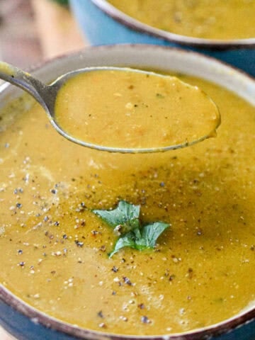 Two bowls of instant pot lentil soup is topped with a cilantro leaf and a spoon is taking some of the soup out of the bowl.