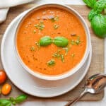 The basil is floating on top of the roasted tomato soup which is on a cutting board.