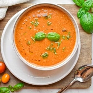 The basil is floating on top of the roasted tomato soup which is on a cutting board.
