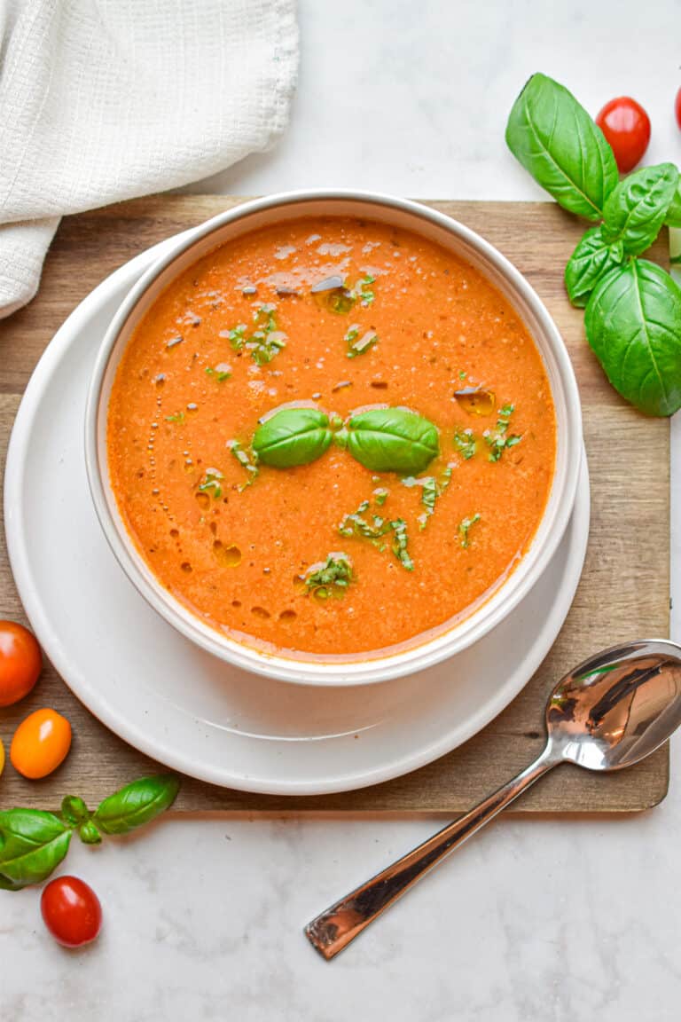 The basil is floating on top of the roasted tomato soup which is on a cutting board.