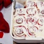 The red velvet cinnamon rolls are in a baking dish with a pie cutter in the baking dish.