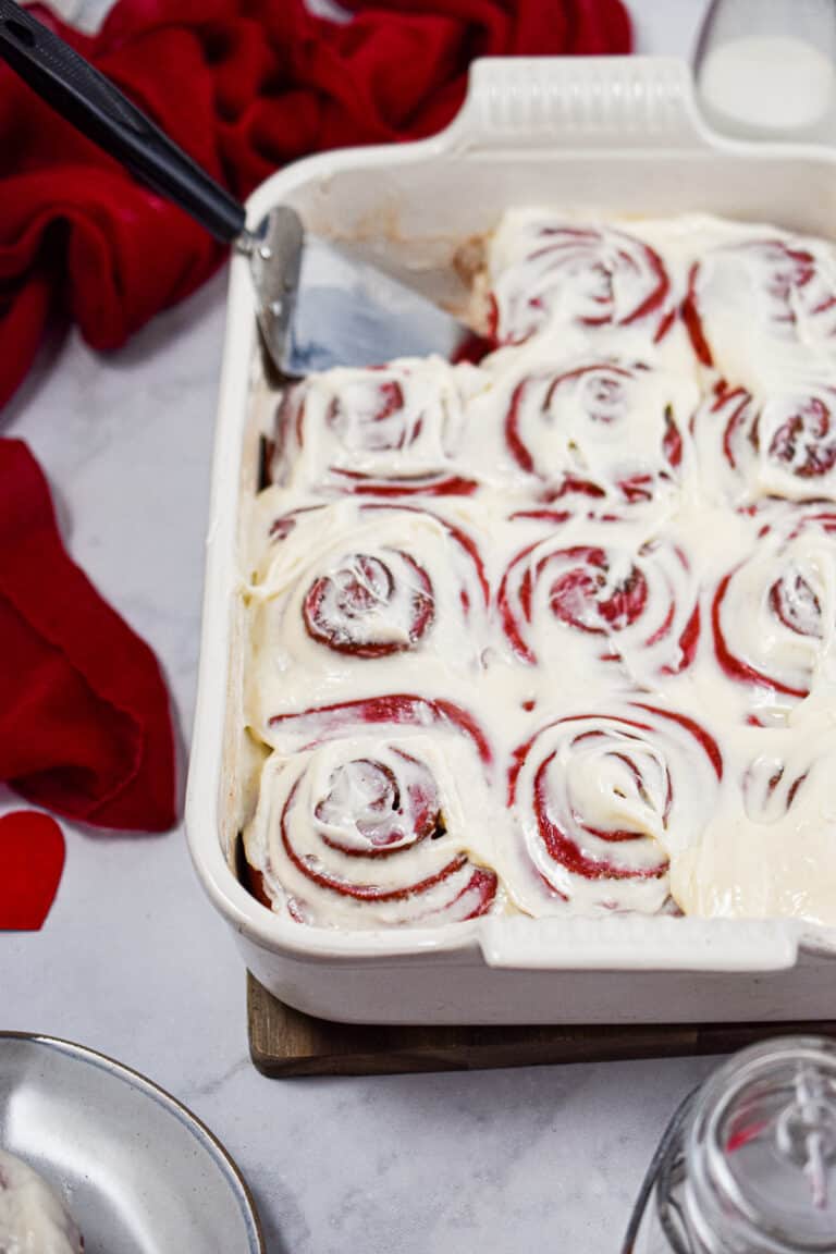 The red velvet cinnamon rolls are in a baking dish with a pie cutter in the baking dish.