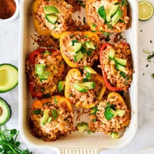 The taco stuffed peppers are in a baking dish surrounded by cilantro and avocado.