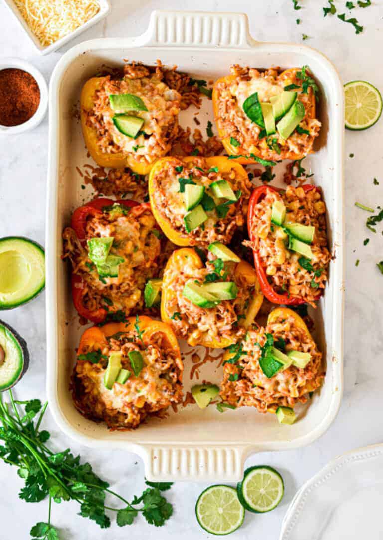 The taco stuffed peppers are in a baking dish surrounded by cilantro and avocado.