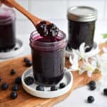 A wooden spoon is lifting the Instant Pot blueberry jam out of a mason jar.