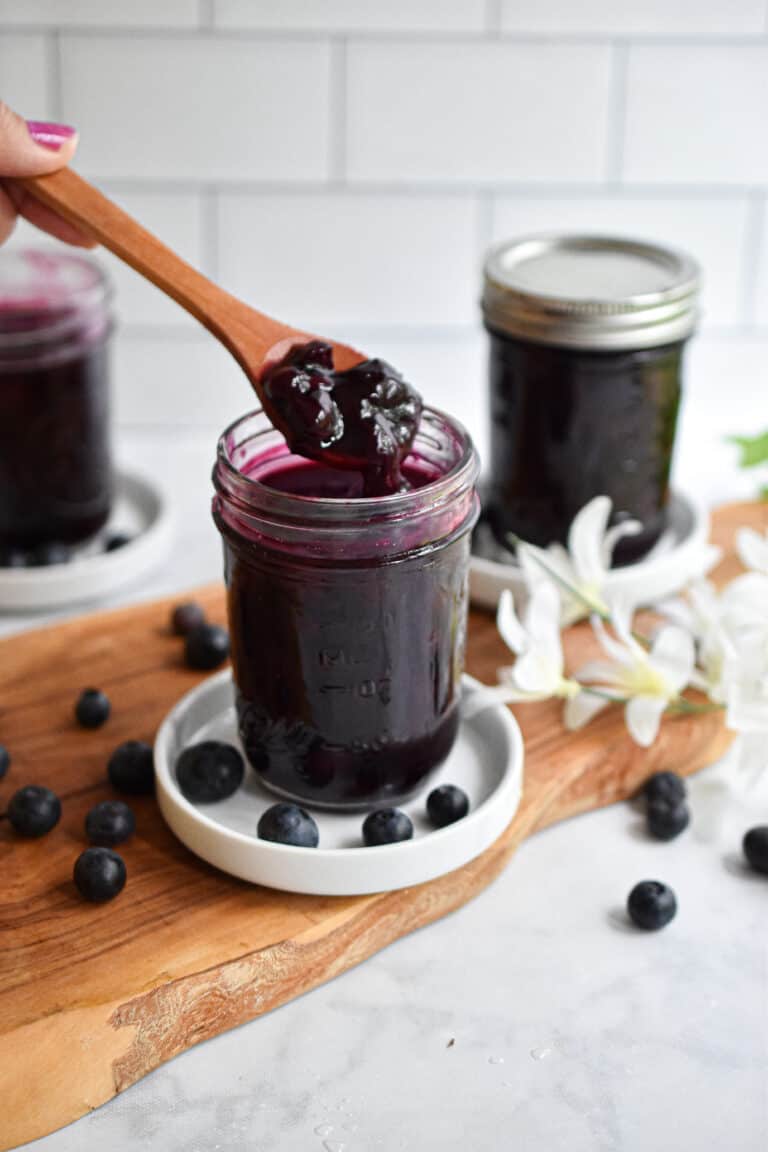 A wooden spoon is lifting the Instant Pot blueberry jam out of a mason jar.