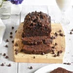 The death by chocolate zucchini bread is on a cutting board surrounded by chocolate chips