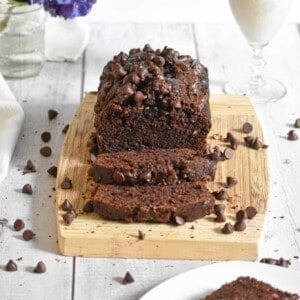 The death by chocolate zucchini bread is on a cutting board surrounded by chocolate chips