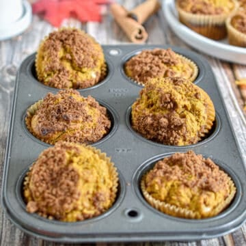 The pumpkin sourdough muffins are in a six pan muffin tin on a wooden backdrop