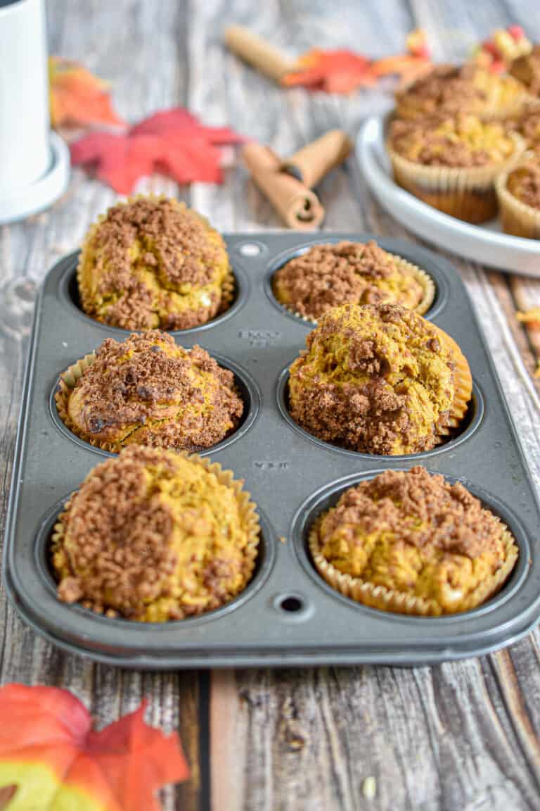 The pumpkin sourdough muffins are in a six pan muffin tin on a wooden backdrop