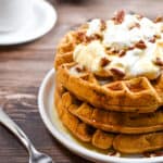 A stack of sourdough pumpkin pancakes is topped with whipped cream and pecans