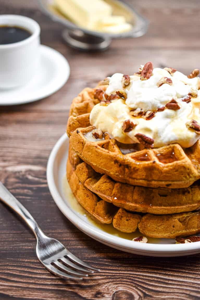 A stack of sourdough pumpkin pancakes is topped with whipped cream and pecans