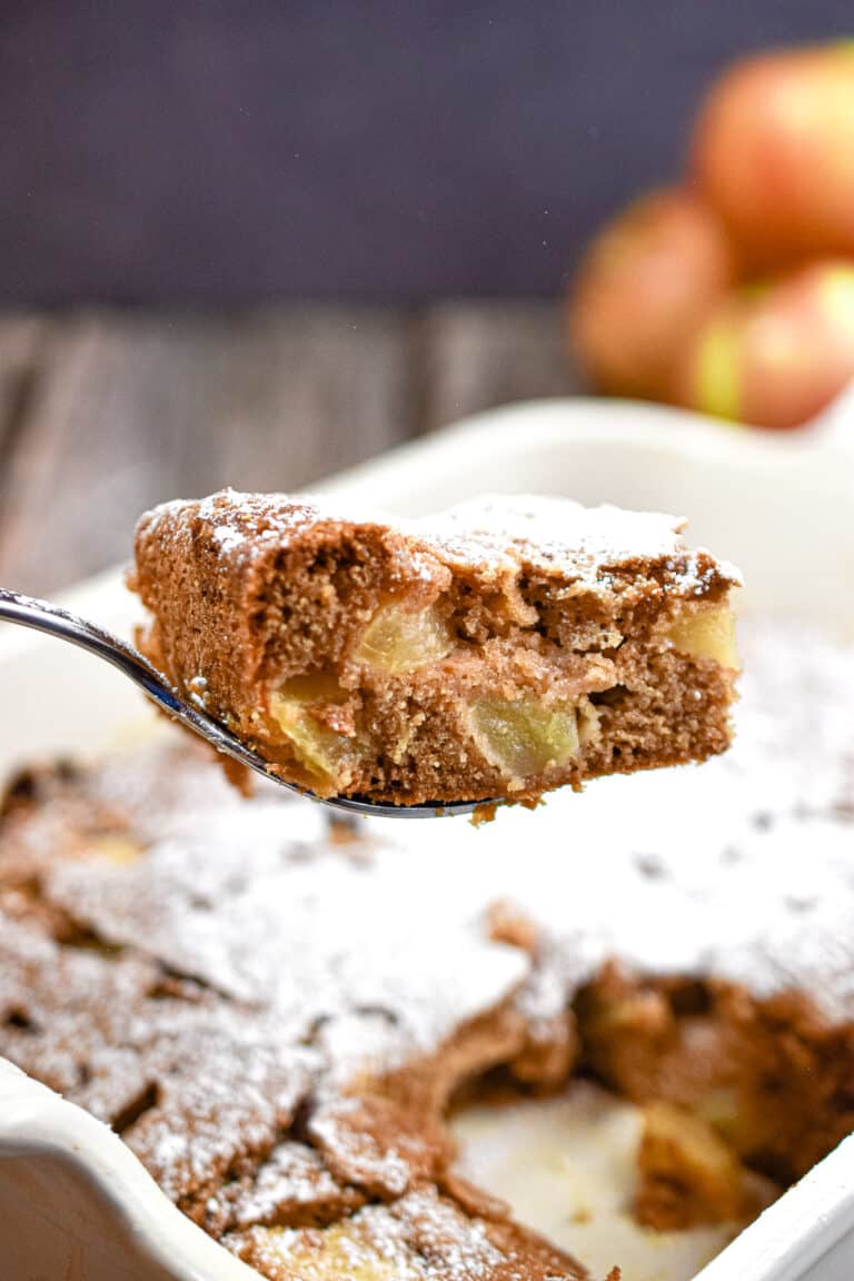 A slice of the all in one apple cake is lifted over the pan