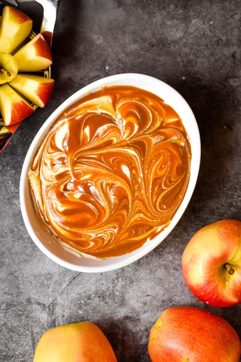 The healthy apple dip is surround by a cut apple and a whole apple