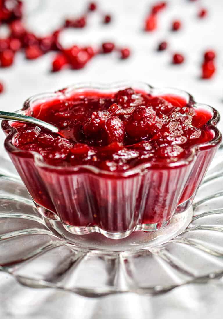 The cranberry sauce is in a glass bowl with oranges in the background
