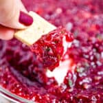 A cracker is dipping into the cranberry jalapeno dip