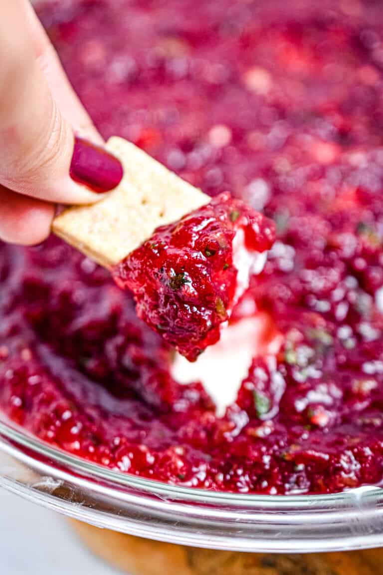 A cracker is dipping into the cranberry jalapeno dip
