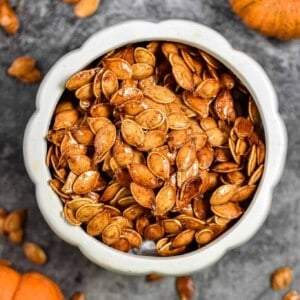 The honey roasted pumpkin seeds are in a large bowl that is surrounded by smaller pumpkin seeds