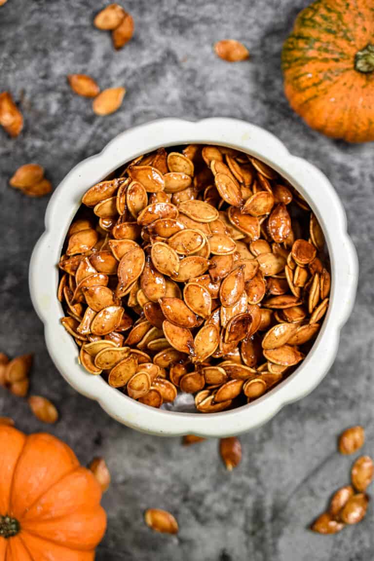 The honey roasted pumpkin seeds are in a large bowl that is surrounded by smaller pumpkin seeds