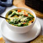 The Instant Pot Zuppa Toscana is in a bowl on a plate with a bread basket in the background