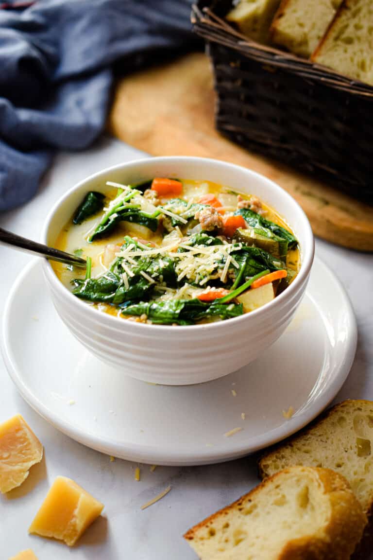 The Instant Pot Zuppa Toscana is in a bowl on a plate with a bread basket in the background