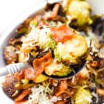 A spoon is lifting the roasted brussel sprouts with bacon and parmesan