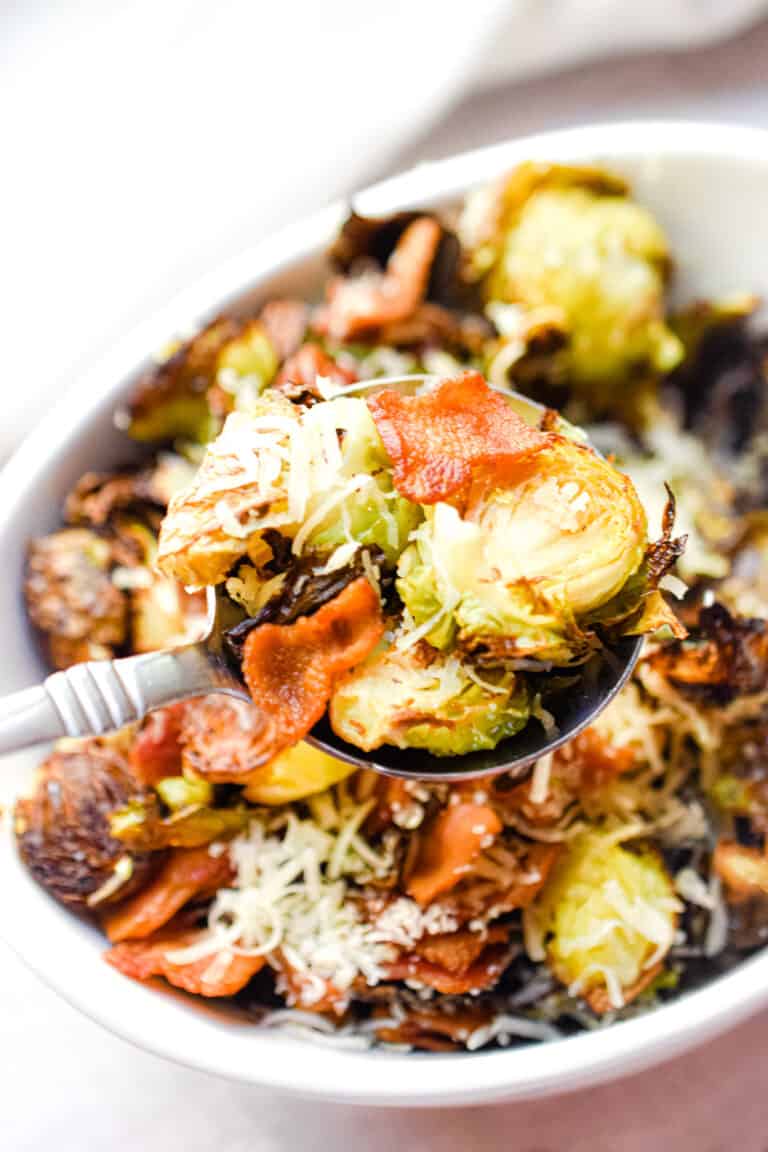 A spoon is lifting the roasted brussel sprouts with bacon and parmesan