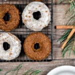 Six baked gingerbread donuts are on a wire rack with one donut on a plate