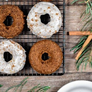 Six baked gingerbread donuts are on a wire rack with one donut on a plate