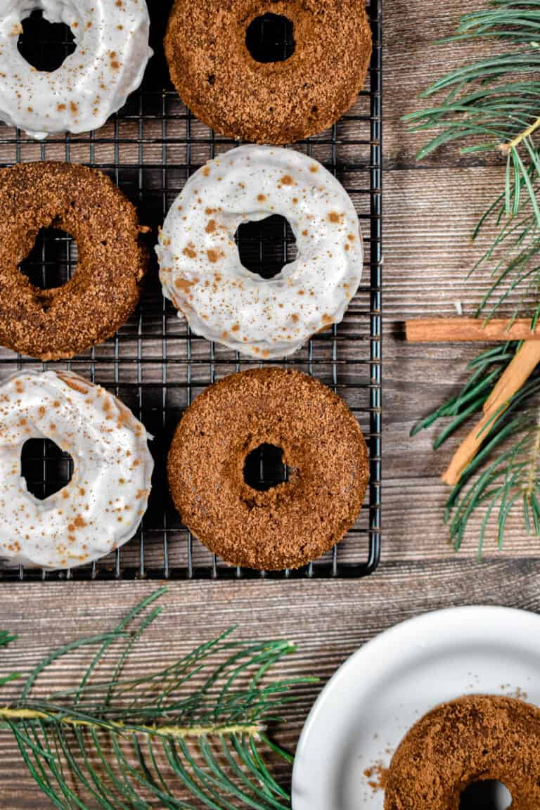Six baked gingerbread donuts are on a wire rack with one donut on a plate