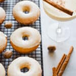 The donuts are on a wire rack with a glass of eggnog next to them