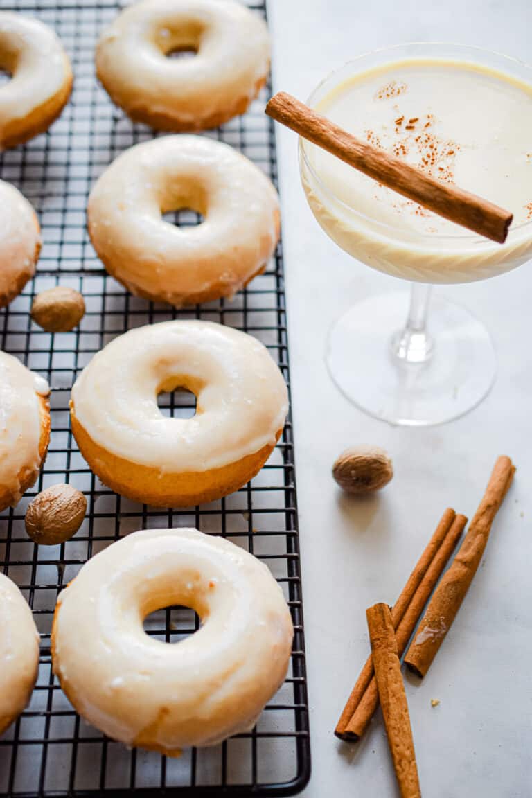 The donuts are on a wire rack with a glass of eggnog next to them