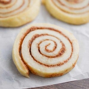 A cinnamon sugar pinwheel cookie is on parchment paper with two cookies behind it.