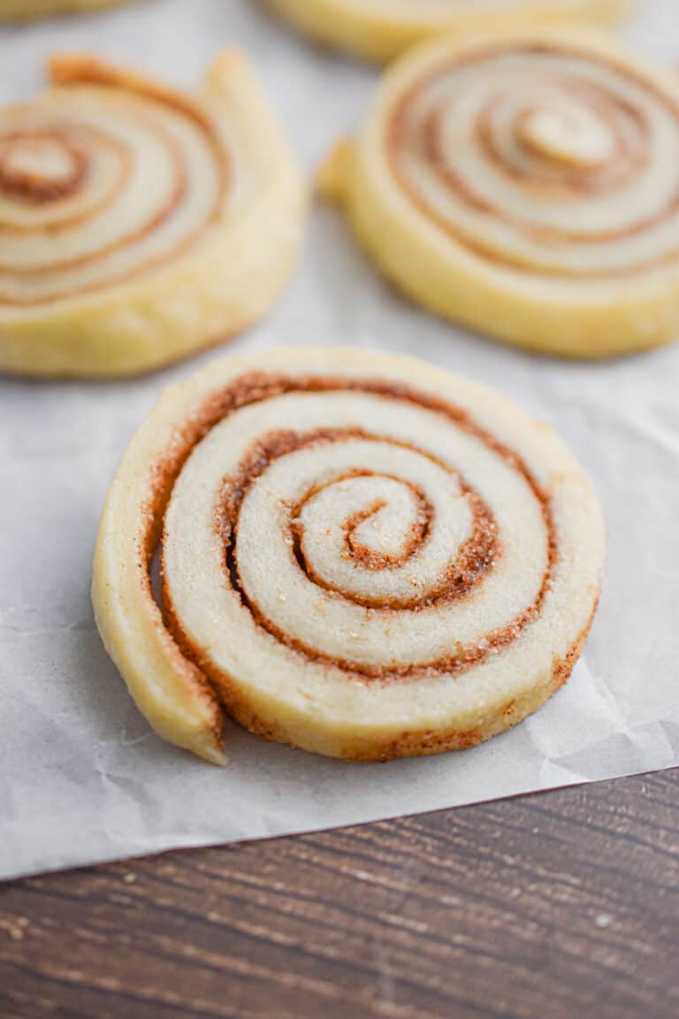 A cinnamon sugar pinwheel cookie is on parchment paper with two cookies behind it.