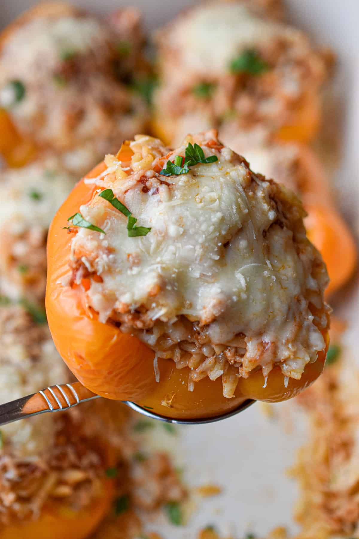 A spoon is holding one of the chicken parmesan stuffed peppers.
