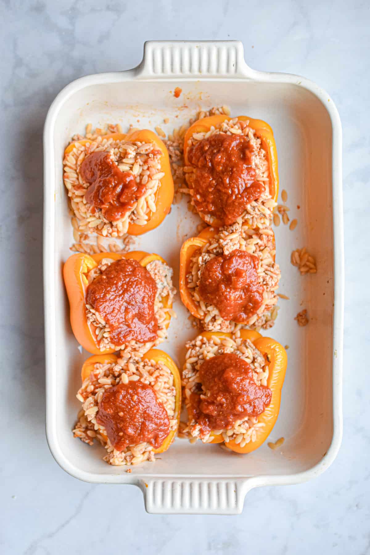 The tomato sauce is spread over the chicken parmesan stuffed peppers.