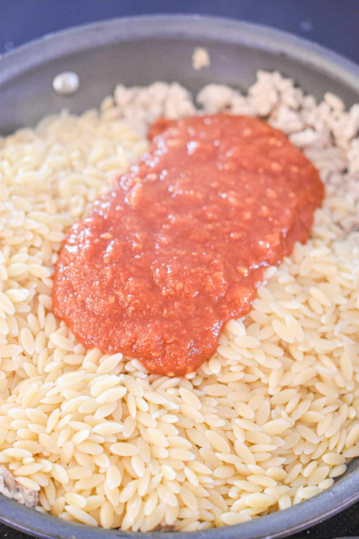 The tomato sauce is being mixed into the cooked orzo.