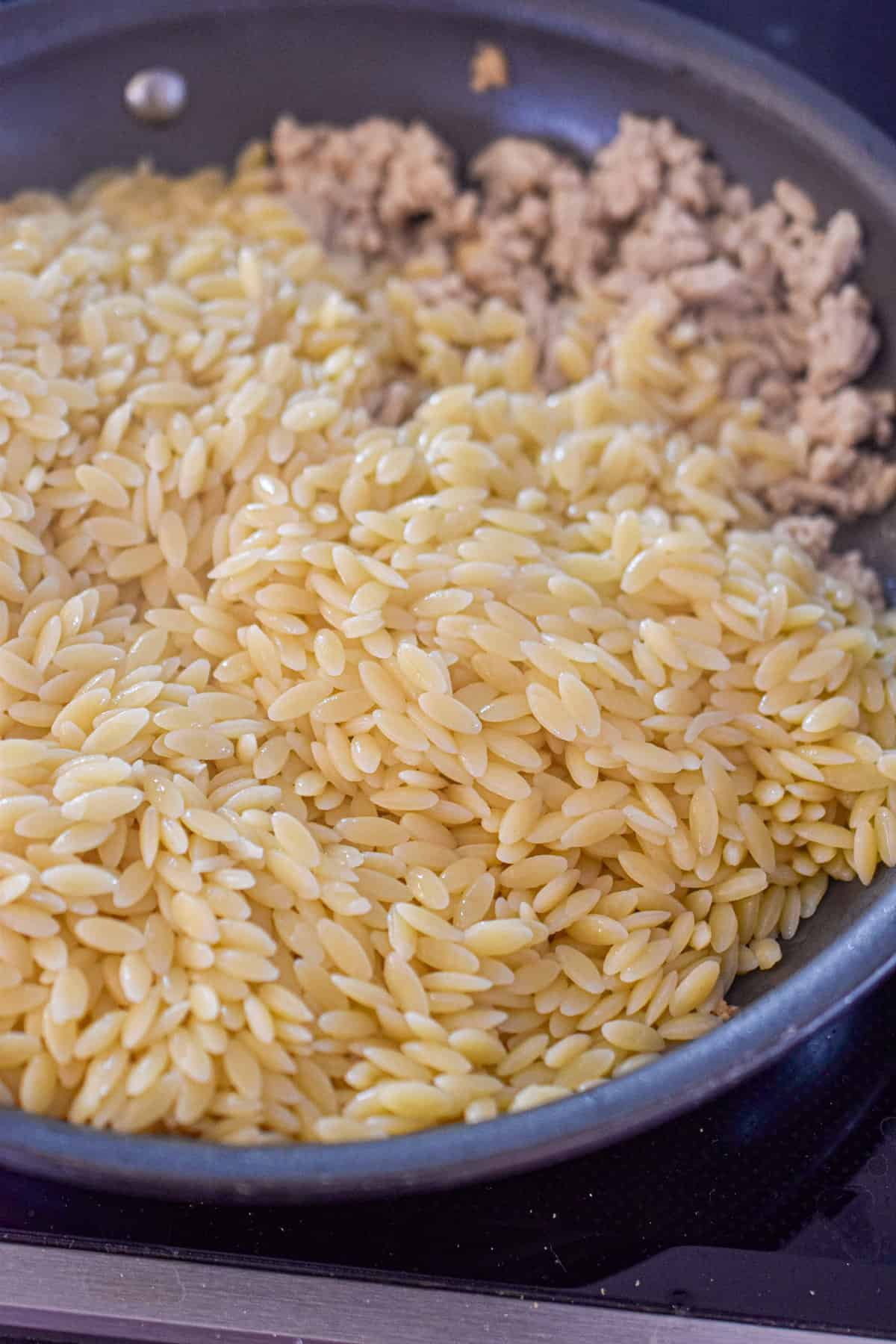 The orzo is added to the sauté pan.