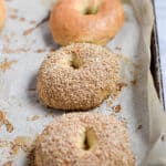 Two sesame seed Instant Pot bagels are on a baking sheet with two other Instant Pot bagels that are plain.