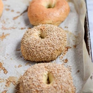 Two sesame seed Instant Pot bagels are on a baking sheet with two other Instant Pot bagels that are plain.