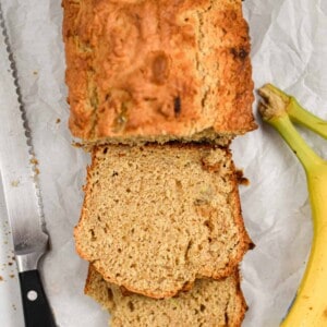 The slices of sourdough discard banana bread are shown with bananas on the right side and a serrated knife on the left side of the loaf.