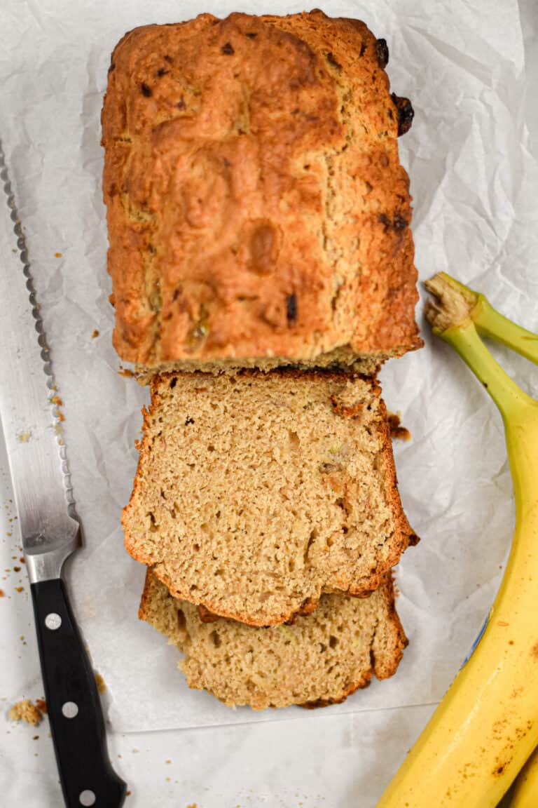 The slices of sourdough discard banana bread are shown with bananas on the right side and a serrated knife on the left side of the loaf.