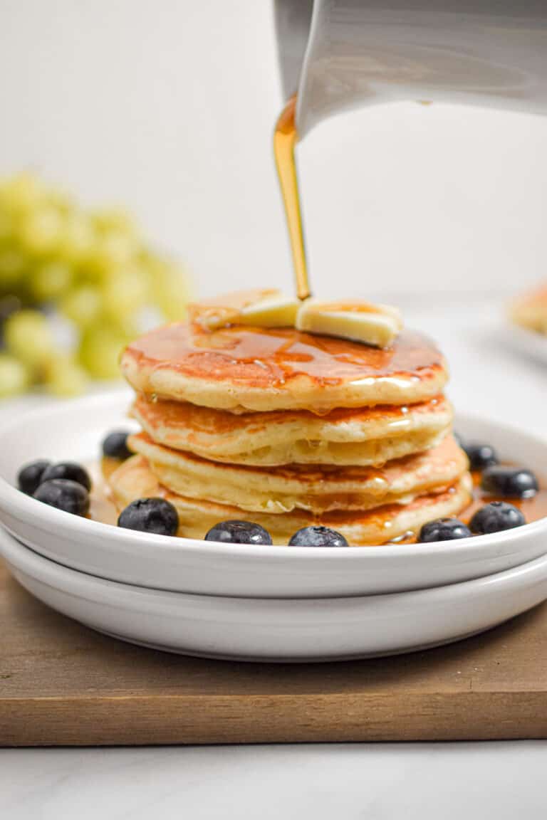 Maple Syrup is being poured over a stack of sourdough discard pancakes.