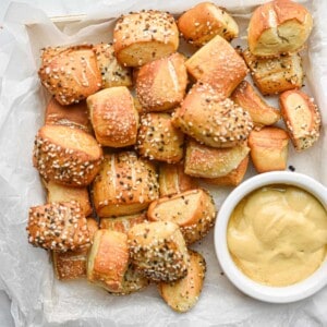 The sourdough pretzel bites are on a square plate with a bowl of mustard on the plate.